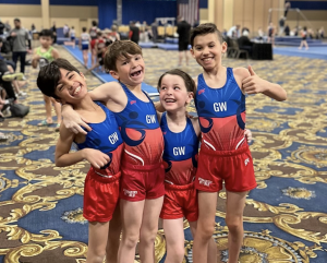 4 gymnasts boys hugging and smiling in their blue and red uniforms