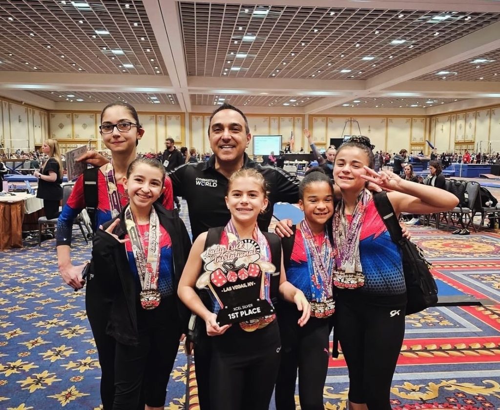 5 gymnasts and their coach posing for picture. Awards and medals on gymnasts after competition.