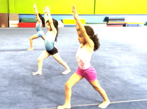 3 girls in a lunge position doing gymnastics on a blue floor