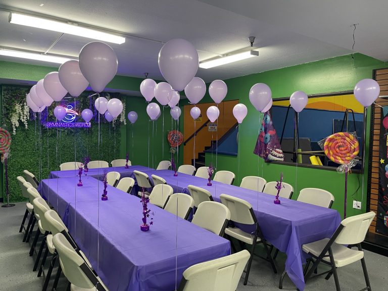 Birthday Party room with green background and purple table decorations and setup. Purple balloons.