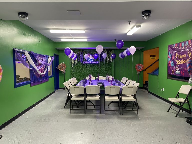 Birthday Party room with green background and purple table decorations and setup. Purple balloons.