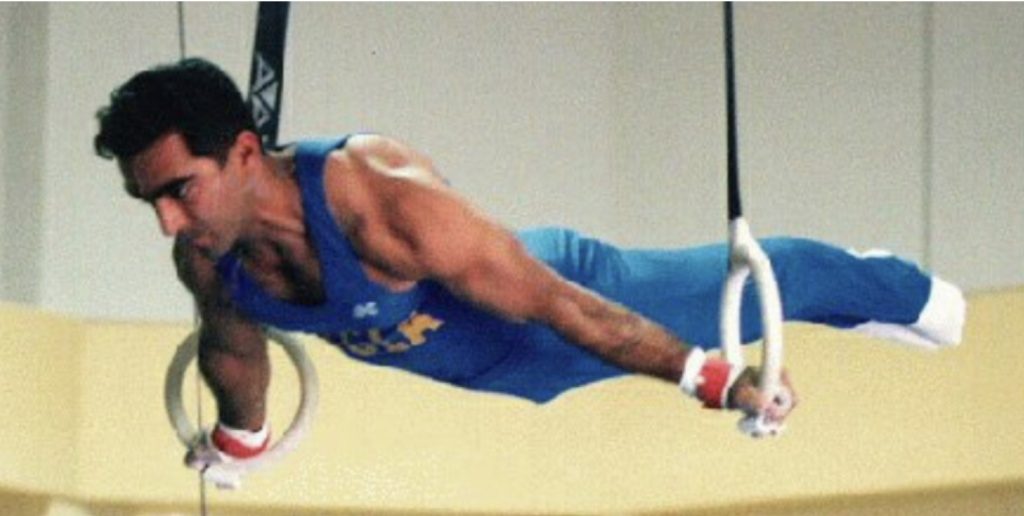 Freddy Behin a UCLA gymnast performing a maltese on rings wearing blue UCLA competitive uniform.